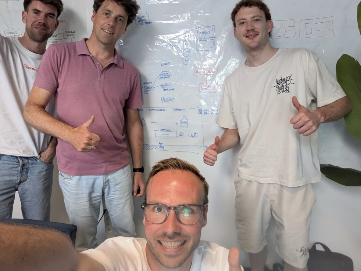 Groepsfoto van vijf mensen voor een whiteboard met uitgewerkte ideeen.
