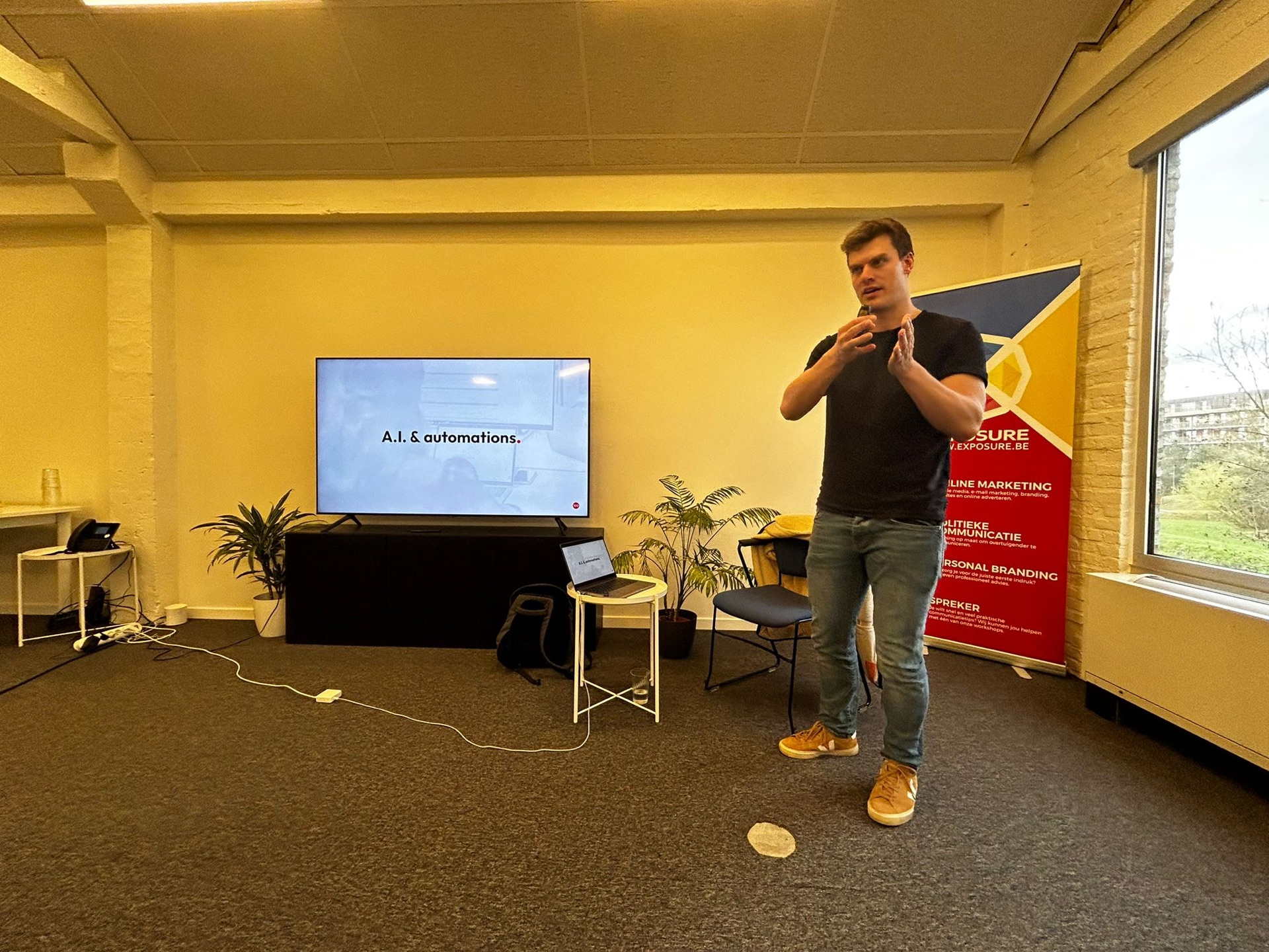 Spreker in een zaal naast de banner van Exposure, op het scherm A.I. en automations.