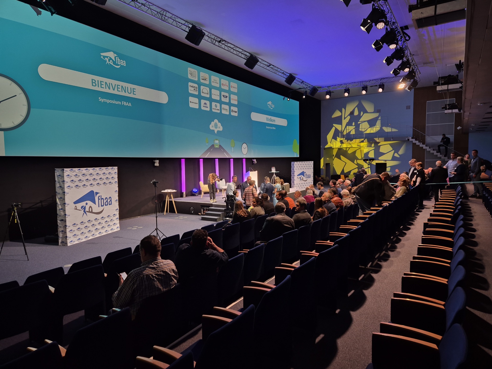 Auditorium met publiek en het welkomstscherm van het FBAA-symposium.