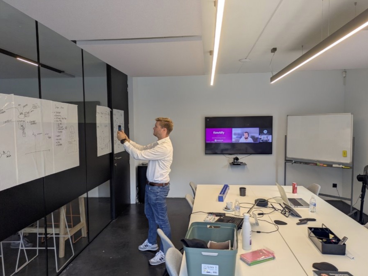 Iemand tekent een proces uit op een whiteboard, met de videocall op het scherm.
