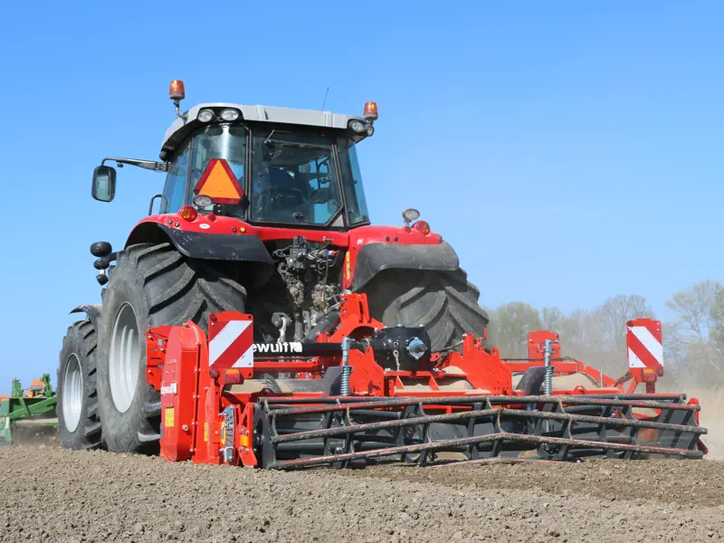 Rode tractor met een rode Dewulf-bodembewerkingsmachine op een pas bewerkt veld.