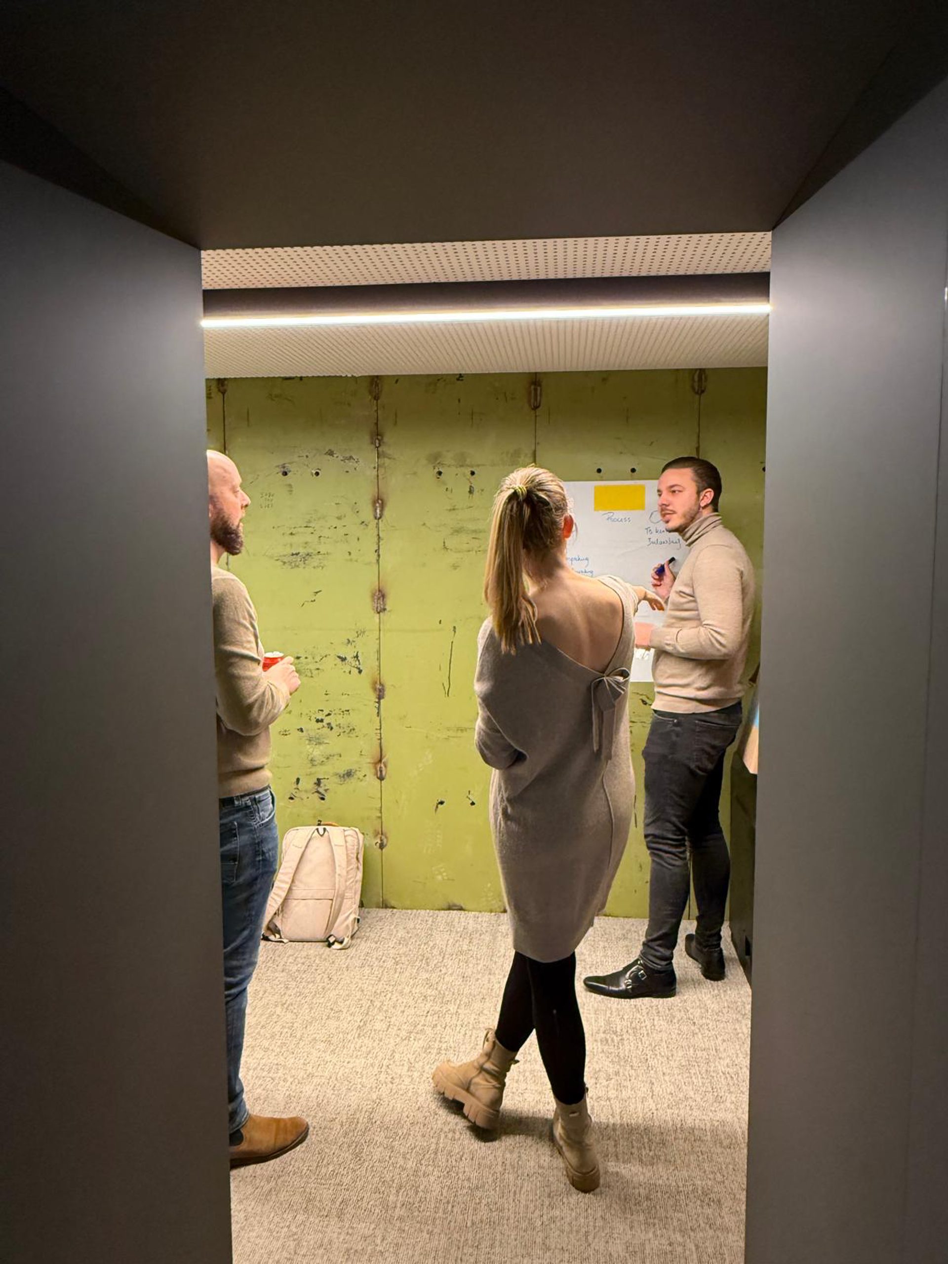 Werksessie in een oude kluis met groene wanden, gezien door de deuropening.