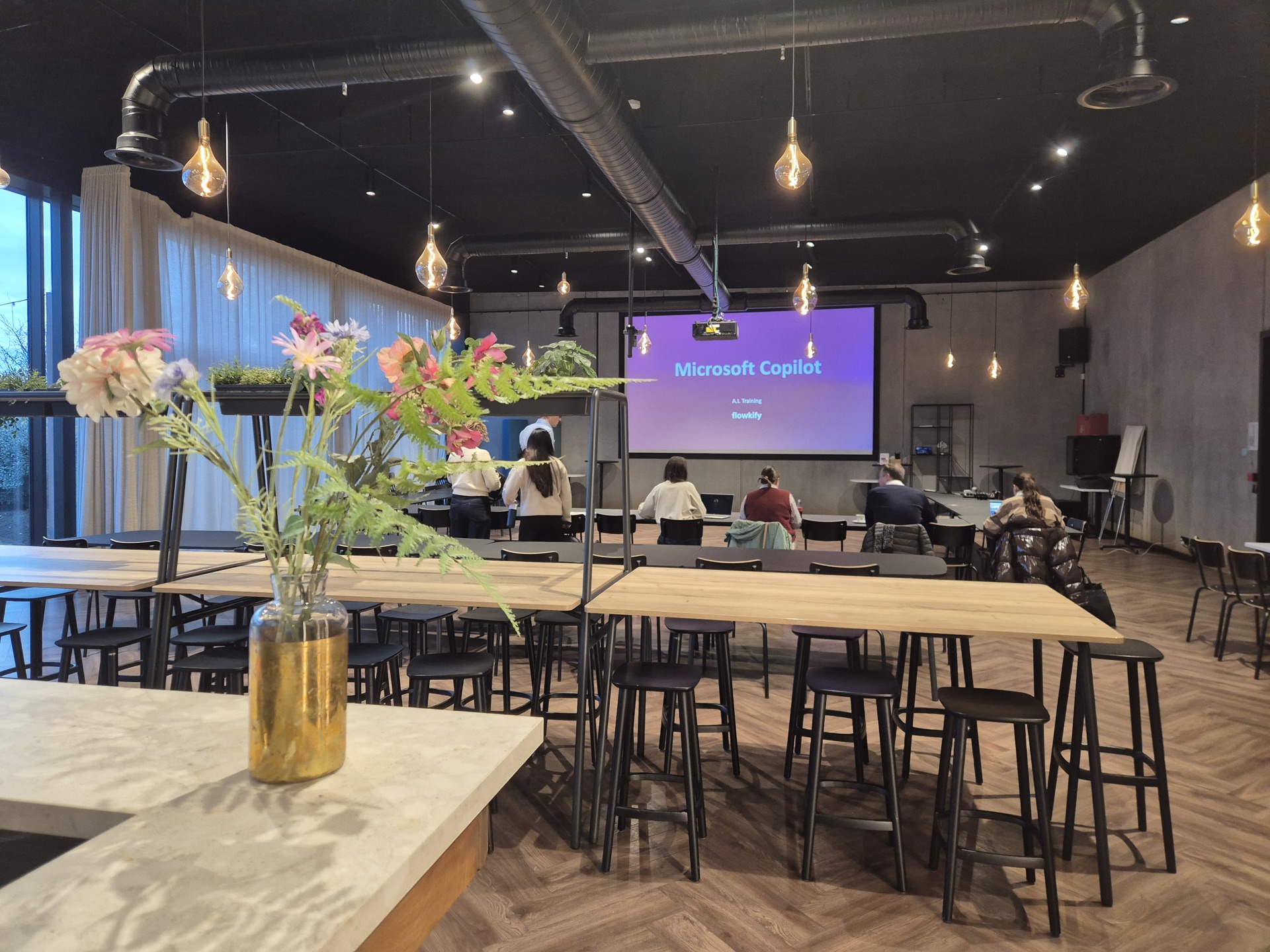 Zaal met hoge tafels en een scherm met de titel Microsoft Copilot.