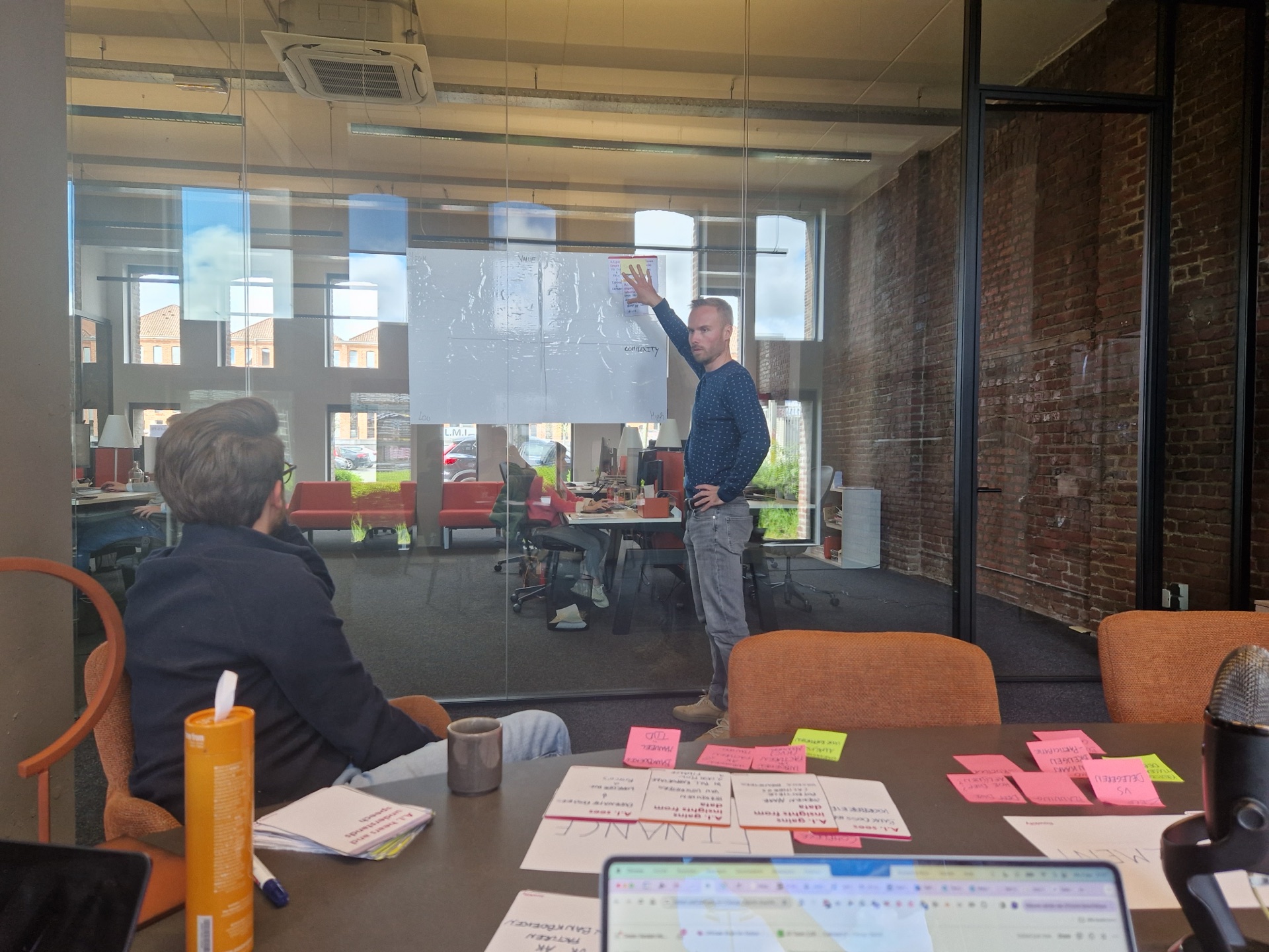 Werksessie met post-its op tafel en iemand die op een whiteboard schrijft.