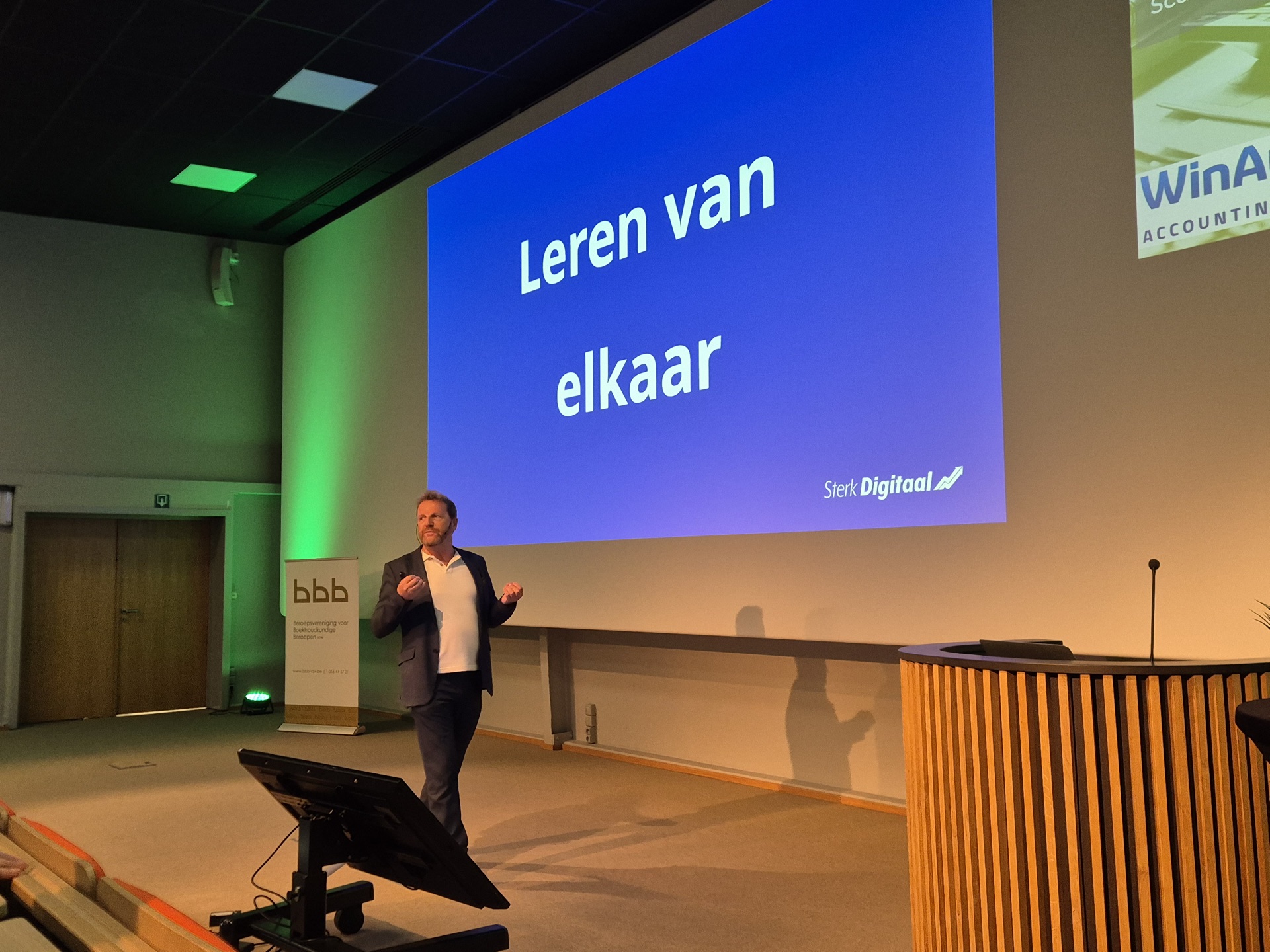 Spreker op een podium voor een slide met Leren van elkaar.
