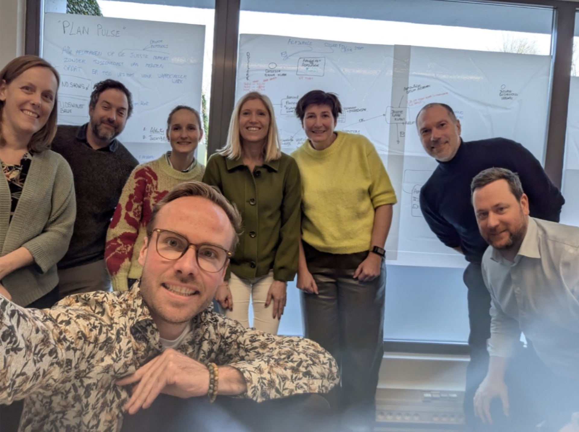 Groepsfoto voor een whiteboard waarop Plan Pulse staat geschreven.