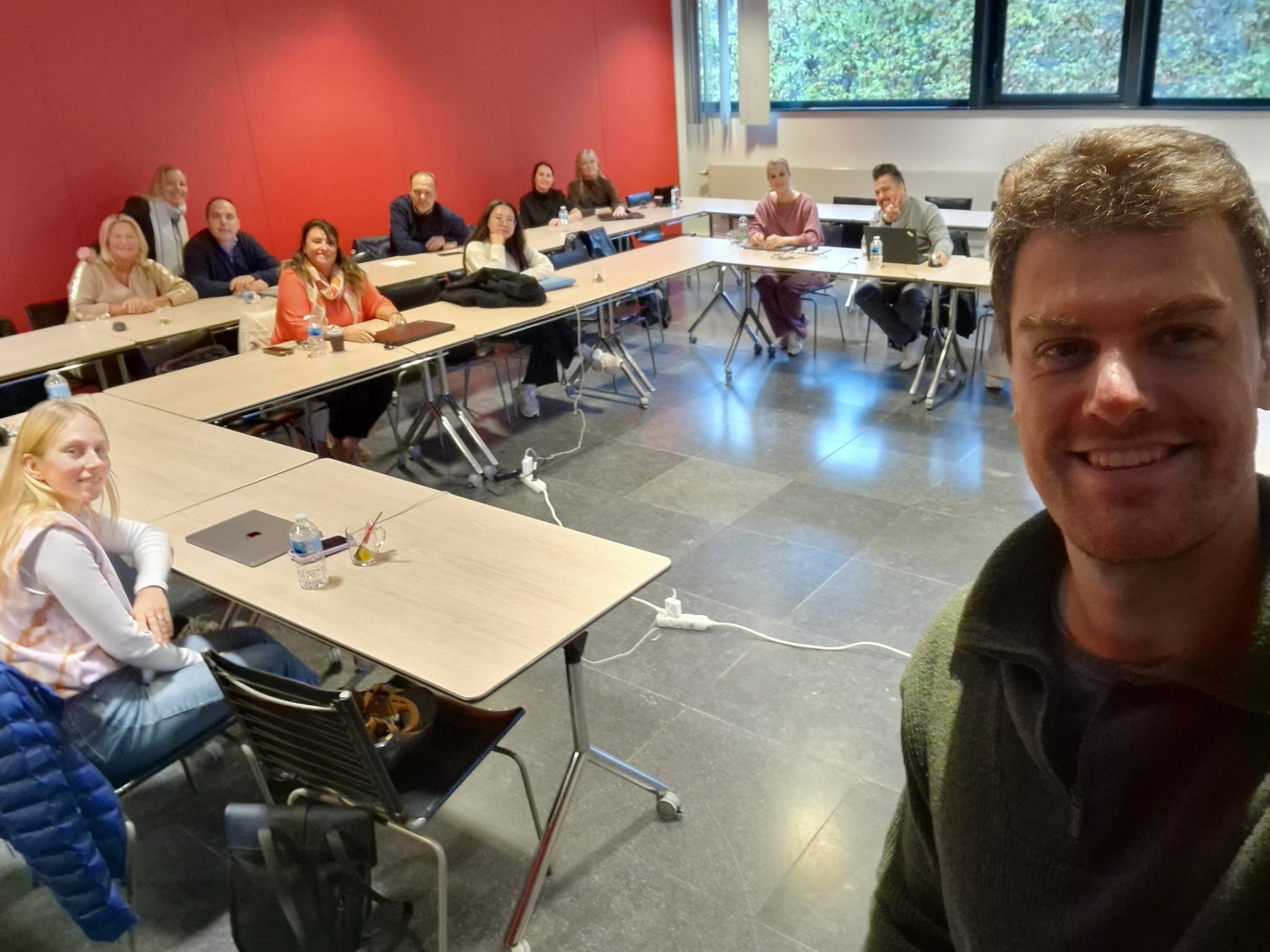 Een twaalftal deelnemers aan tafels in een leslokaal.